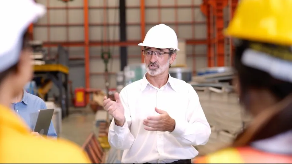 A senior engineer in a hard hat explaining something to his team on the factory floor